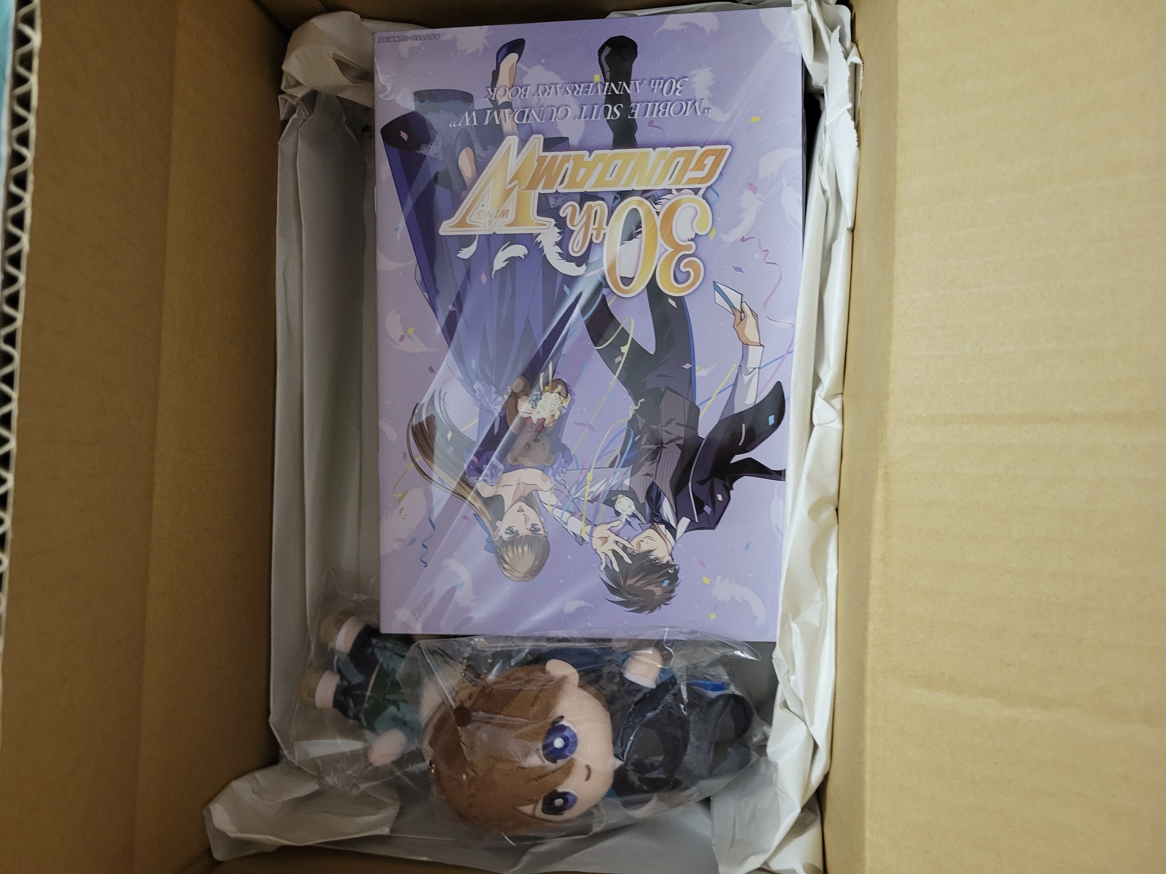 Cardboard box wih Gundam wing 30th anniversary book and Heero plus Duo plush shwoing.